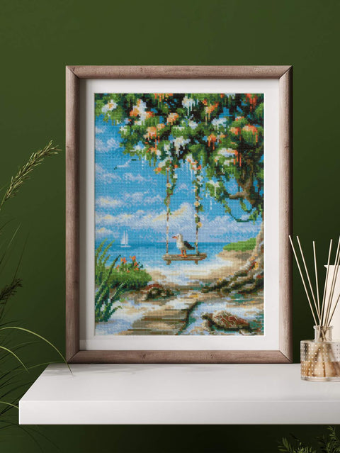 Siuvinėtas paveikslas jūros peizažas rėme, 30×40 cm, sodrūs mėlyni ir žali tonai, eksponuotas ant balto lentynos