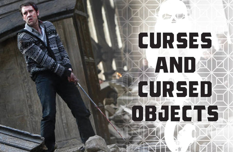 knyga Curses and Cursed Objects — minkštas viršelis su baltu kaukolės raštu, tamsiu geomatriniu fonu ir veikėjo scena fone