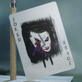 Drobė su Joker piešiniu, balta fono ir juodais teptuko brūkšniais, 30×40 cm, kampu parodyta tekstūra