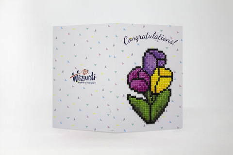 Atvirukas Wizardi atvertas, baltas fonas su spalvotais trikampiais ir pikselių gėlių mozaika (violetinė, geltona, žalia) bei „Congratulations“ užrašu dešinėje