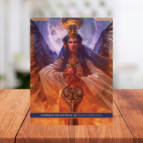 Dienoraštis Goddess Isis Alana Fairchild – minkštu viršeliu su Isis dievės iliustracija, šiltai oranžiniai tonai, stovi ant medinio stalo