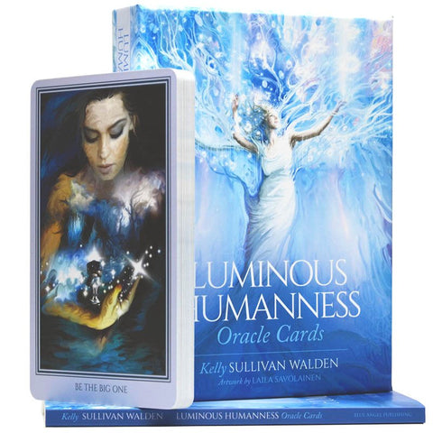 Luminous Humanness oracle kortos su mėlynu dėklu ir atversta iliustruota korta, aut. Kelly Sullivan Walden, iliustr. Laila Savolainen