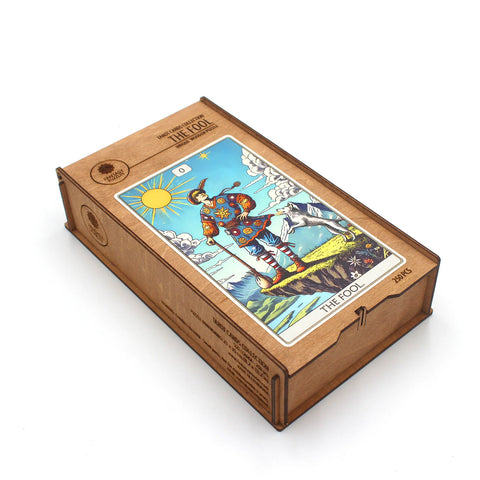 Tarot kortos medinėje dėžutėje su The Fool viršeliu, ryškus spalvotas kortos piešinys, parodytos iš viršaus kampu