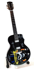 elektrinė gitara juoda su Guns N' Roses kaukolės grafika ir grupės parašais, blizgus korpusas ant stovo