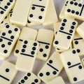 Domino kauliukai kreminės spalvos su iškiliais juodais taškais, arti sudėliota kompozicija pabrėžia paviršiaus faktūrą ir taškų profilį