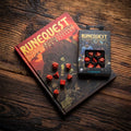 Runquest Bestiary knyga su raudonu kietu viršeliu ir derančiu raudonų poliedrinių kauliukų rinkiniu dėžutėje ant medinio stalo