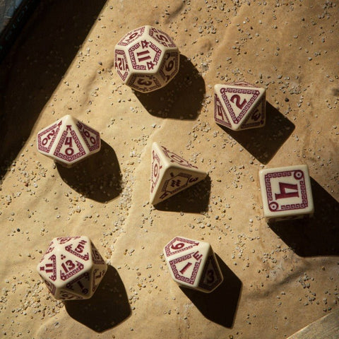 RPG kauliukai 7 dalių rinkinys kremine baze ir bordo skaitmenimis, polyedriniai kauliukai išdėstyti ant smėlingo popieriaus, fotografuoti viršaus kampu