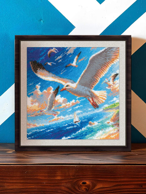 kryželių paveikslas su žuvėdrų ir jūros motyvu, rėmintas tamsiu rėmu, apie 40×50 cm, rodomas iš priekio ant lentynos