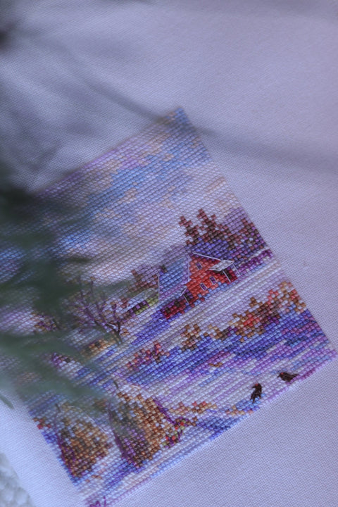 Kryželių rinkinys: mažas žiemos peizažo kvadratas su raudonu nameliu ir pastelinių violetinių bei mėlynų siūlių raštu, fotografuotas iš viršaus