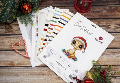 Kryželių siuvinėjimo rinkinys Lucas Christmas Gifts su spalvotomis siūlų kortelėmis, modelio schemomis ir mažuoju dinozauru su Kalėdų kepure