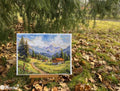 Drobė Meregka 30×40 cm su kalnų peizažu ir nameliu, ant mažo stovelio lauke, ryškios spalvos ir tekstūra