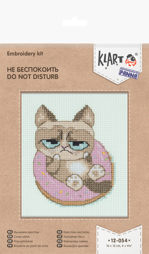 Siuvinėjimo rinkinys Klart: 10×12 cm, pakuotėje matoma piktos katės dizainas ant rožinės spurgos, kryželių variantas