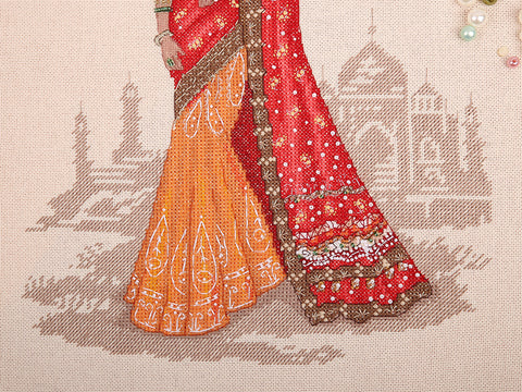 Sari su oranžiniu sijonu ir raudonu šalu, arti rodomos siuvinėjimo, karoliukų ir krašto detalės, fone Taj Mahal motyvas