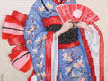 Siuvinėtas geišos paveikslas artimas planas: mėlyno kimono gėlės su karoliukais, raudonas vėduoklės ir kaspino akcentas