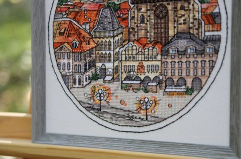 Siuvinys — apvalus miesto peizažas pilkame mediniame rėme, detali kryželių kompozicija su gatvės žibintais