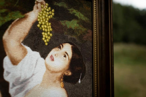 Paveikslas rėme, arti priartinta drobės tekstūra ir moters portreto detalė su geltonomis vynuogių kekėmis