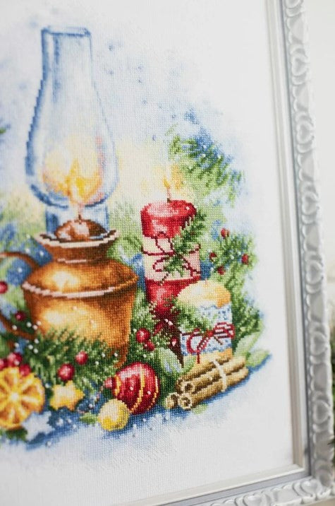 kryželiu siuvinėtas paveikslas su raudonomis žvakėmis, žalumynais ir bronzine lempa, sidabrinio rėmo kampo priartinimas