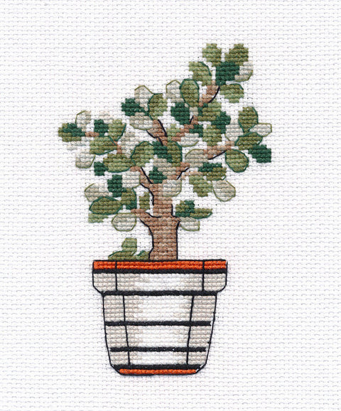 siuvinėtas bonsai su žaliais lapais ir rudu kamienu ant balto vazonėlio su oranžiniu kraštu, artimas priekinis planas, dekoratyvinė tekstilės detalė
