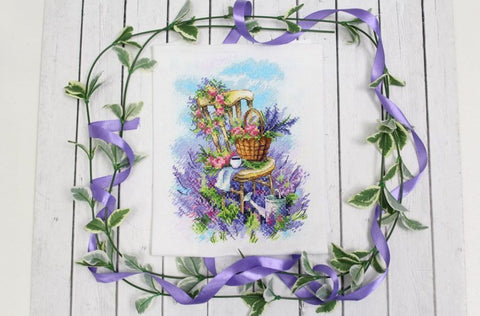 Siuvinėjimo rinkinys su levandų motyvu: kėdė su pintine gėlėmis ant balto audinio, pakuotė su violetine juostele