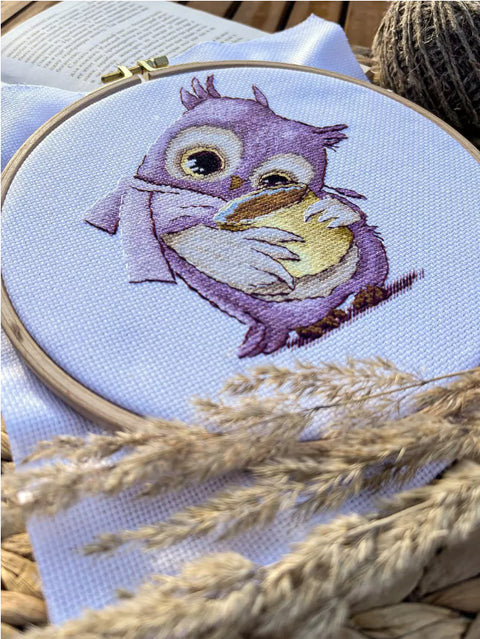 Siuvinėjimo rinkinys su violetine pelėda ant medinio lankelio, arti parodytos siūlių, atspalvių ir audinio tekstūros detalės