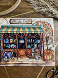 kryželių siuvinys rudeniška „Magic Shop“ vitrina su žalia dryžuota markize, moliūgais, prekėmis ant lentynų ir maža katyte