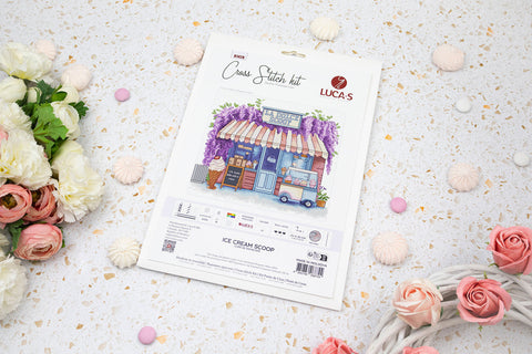 Kryželių siuvinėjimo rinkinys LUCA-S „Ice Cream Scoop“ — priekinis viršelis su ledų parduotuvės motyvu ir komplektacijos etiketė, plokščiai fotografuotas tarp gėlių