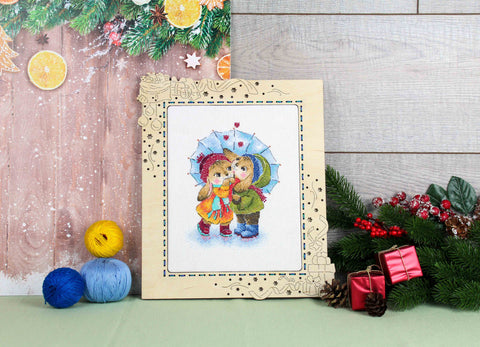 Siuvinėjimo paveikslėlis 20x25 cm mediniame šviesiame šventiniame rėme — spalvingi vaikų portretėliai po mėlynu skėčiu