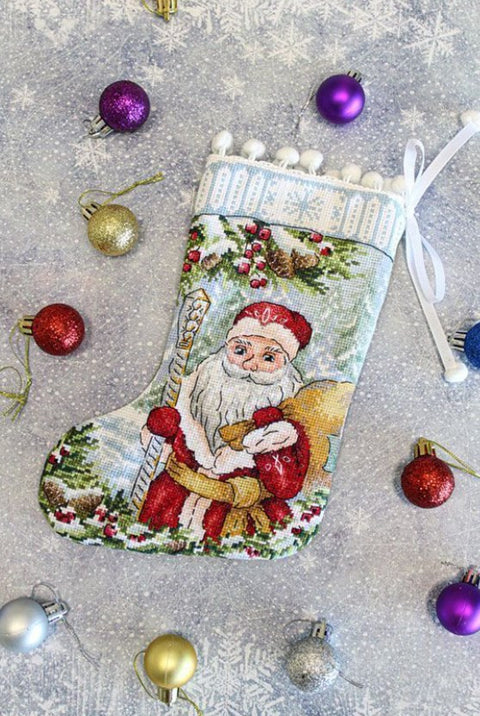Kalėdinė kojinė siuvinėta rankomis su Senelio ir maišo motyvu, šviesiai mėlyna fone, pom‑pom apdaila, skirta kabinti prie židinio ar eglutės