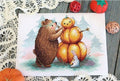 Kryželių rinkinys: rudeniškas lokys dėlioja moliūgų figūrą ant balto audinio, 30×24 cm, frontinis kadravimas ir dekoratyvios nėrinės