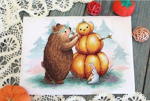 Kryželių rinkinys: rudeniškas lokys dėlioja moliūgų figūrą ant balto audinio, 30×24 cm, frontinis kadravimas ir dekoratyvios nėrinės
