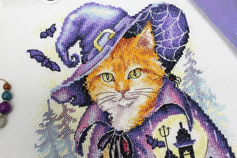 Siuvinėjimo rinkinys — arti kadro oranžinė katė su violetine raganos skrybėle, apsiaustu ir papildomais karoliukais