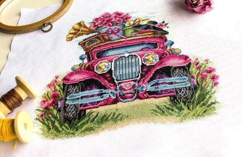 Siuvinėjimo rinkinys rožinio retro automobilio motyvu, arti parodytas detalus kryželių raštas su siūlais ir lankeliu