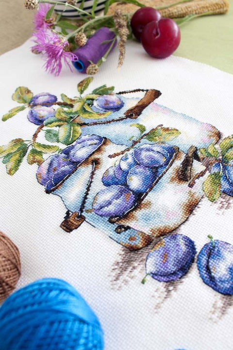 Kryželių siuvinėjimo rinkinys, artimas kampas su violetinėmis slyvomis ant dekoratyvinio maišelio ir siūlų kamuoliukais
