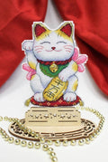 Maneki-neko siuvinėta statulėlė, balta su auksinėmis dėmėmis ir žaliu kaklaraiščiu, ant medinio žvaigždžių pagrindo