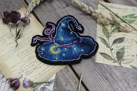 Siuvinėtas pleistras raganos skrybėlė, tamsiai mėlynas su geltonu mėnuliu ir žvaigždėmis, apie 7×6 cm, artimas kampinis planas