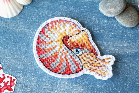 Siuvinėtas pleistras nautilio formos, oranžinės ir raudonos spalvos, apie 8×6 cm, detaliai parodyta siūlų faktūra