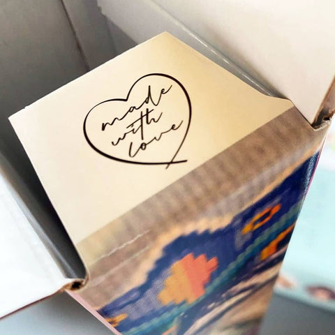 Pakavimo dėžutė su balta viršutine plokšte ir juodu „made with love“ širdies lipduku, artiškas viršaus kampo užfiksavimas