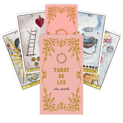 tarot kortos Tarot de Luz rožinė dėžutė su auksiniu ornamentu ir keliomis atverstomis iliustruotomis kortomis, pabrėžiant dizainą ir pakuotę