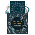 Tarot kortos Trinity Tarot dėžutė su tamsiu viršeliu ir aukso užrašu, išdėstytos virš kelių atverstų kortų