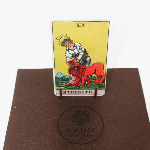 Tarot korta Strength ant mažo stovelio, raudonas liūtas ir geltonas fonas, stovinti ant Fantasy Puzzles rudos dėžutės logotipo