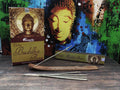 smilkalai Aromatika Buddha Flora su auksinės pakuotės dėže, medine laikikliu ir keliomis lazdelėmis ant stalo