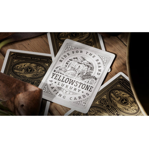 Kortos Yellowstone Luxury baltos su juodais ir auksiniais raštais, arti kampo parodytas priekis su iliustracija ir logotipu, skiriasi nuo dėžutės kadrų